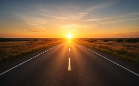 A long, empty road leading toward a sunset in a rural landscape.